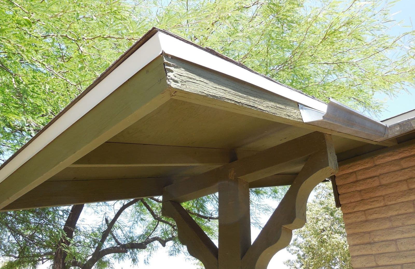 Olive-painted wood porch beam with large curved wood corbel brackets on a post, white drip edge and galvanized gutter over a tan block wall