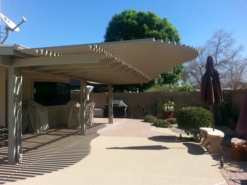 Almond aluminum lattice patio cover with a curved end attached to a house over a paver and concrete patio