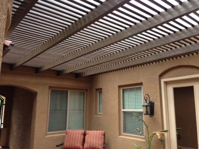 Dark brown aluminum lattice patio cover in a tan stucco courtyard with windows and a lantern