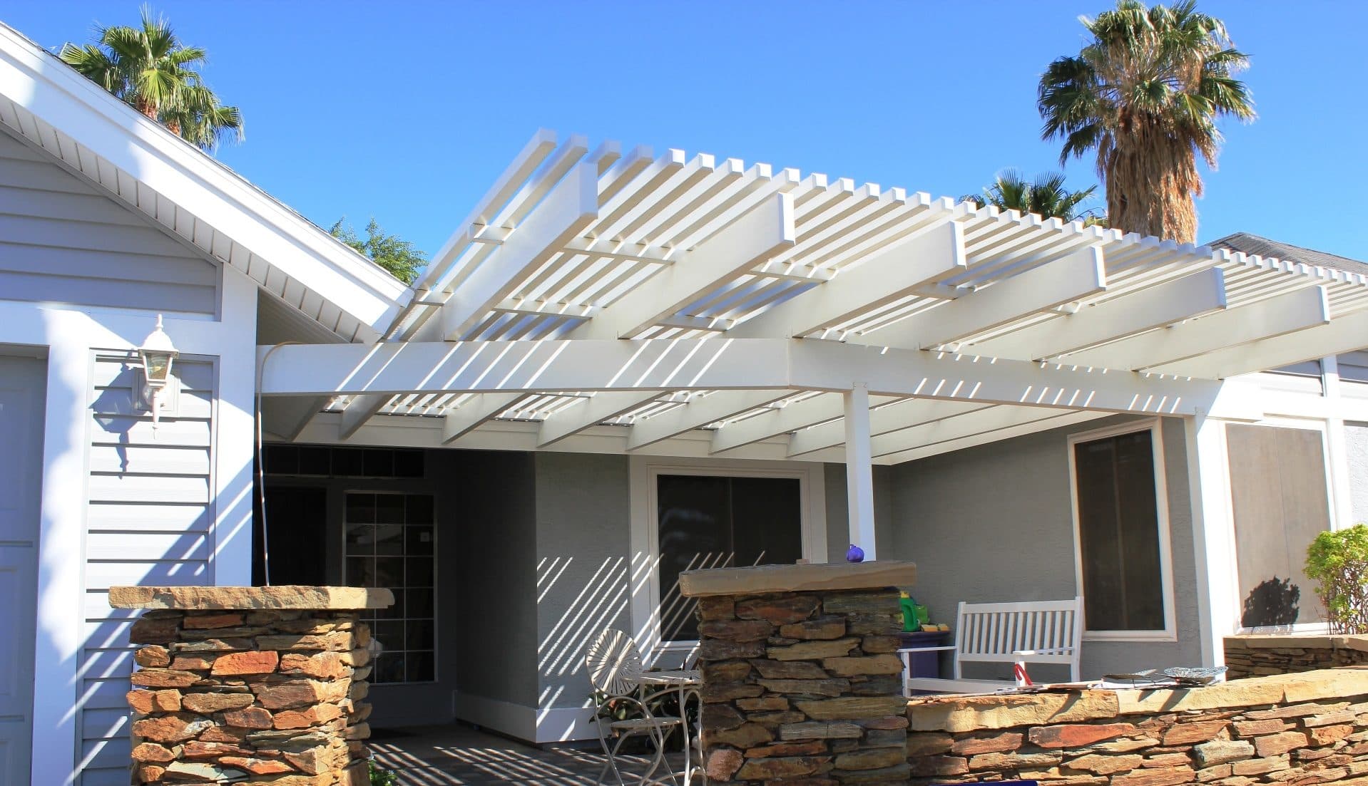 White aluminum lattice entry cover on a grey house with new grey vinyl siding, white soffit and fascia, stacked-stone pillar and palms
